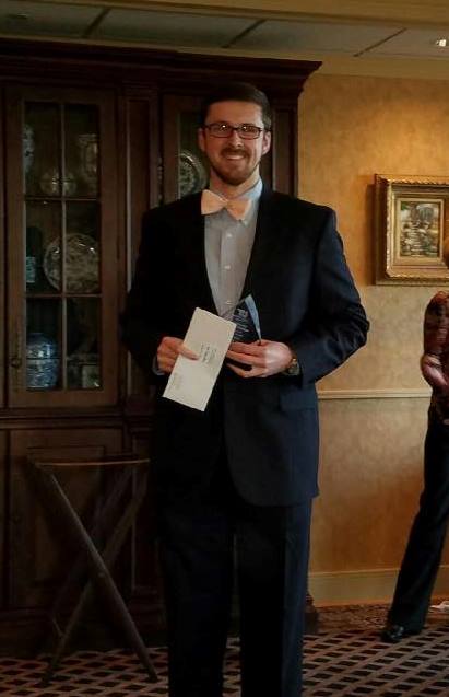 Hugh Smith standing with awards.