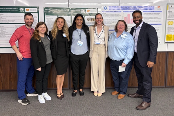 7 male and female residents and faculty standing before a poster presentation