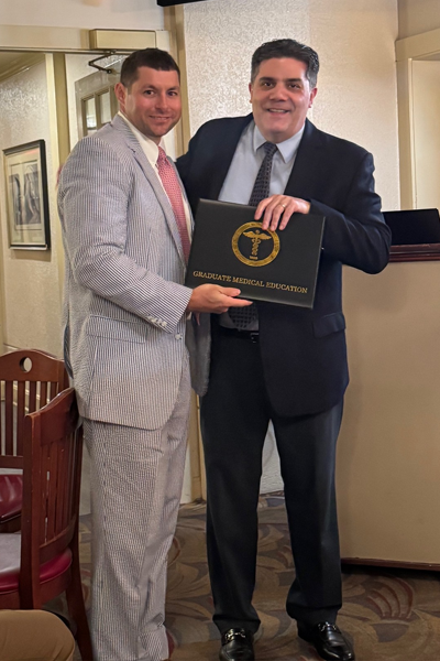 Graduate holding a certificate and faculty posing together