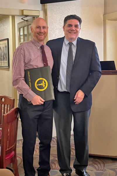 Graduate holding a certificate and faculty posing together