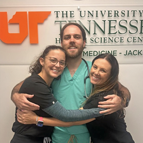 Male and two female residents hugging in front of an indoor UTHSC sign