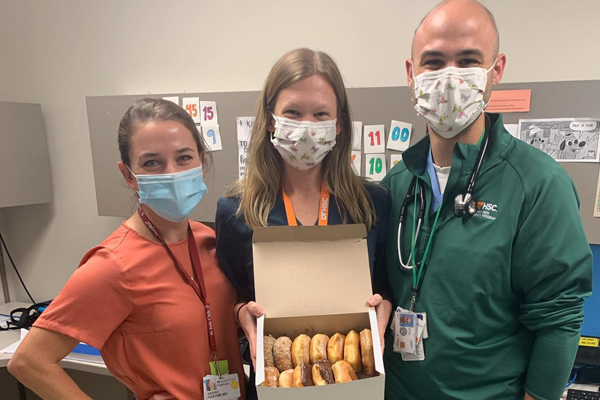 A female resident in a mask, a female resident in a mask holding a box of donutes, and a male resident wearing a mask