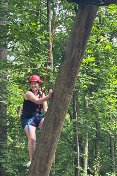 Female resident climging a log at a team building session in the woods