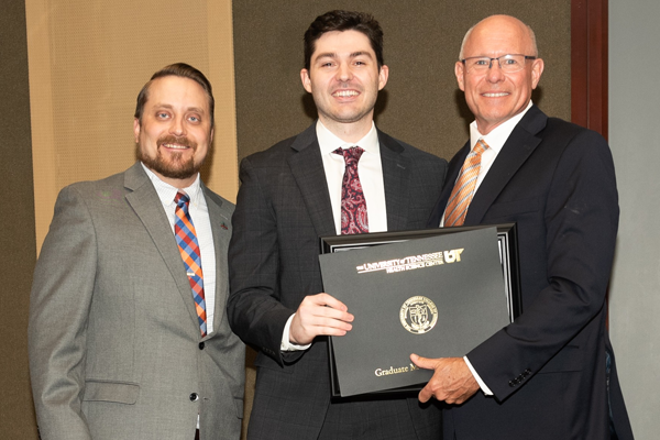 Resident holding a certificate with faculty at graduation