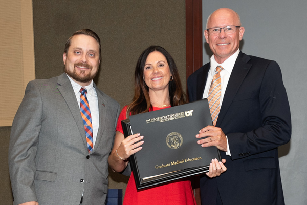 Resident holding a certificate with faculty at graduation