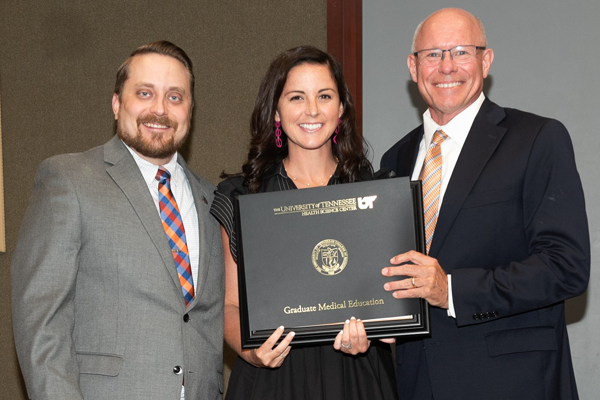 Resident holding a certificate with faculty at graduation