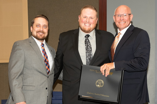 Resident holding a certificate with faculty at graduation