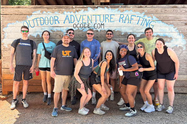 Residents posing outdoors in front of a wooden outdoor adventure rafting sign