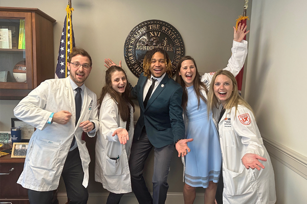 Five residents in an office in front of a seal and flag