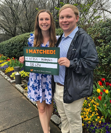 Resident with spouse holding match day sign