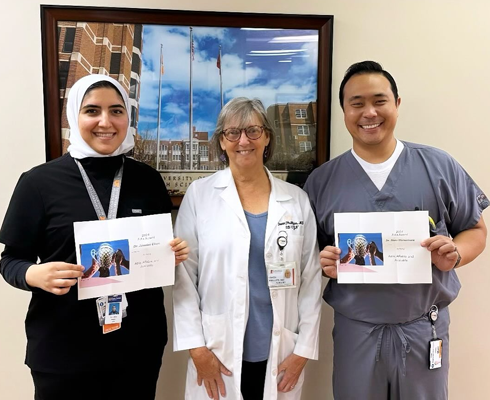 Residents holding certificates on each side of a faculty member