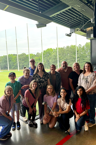 Fellows, family and faculty posing before the driving range at Top Golf
