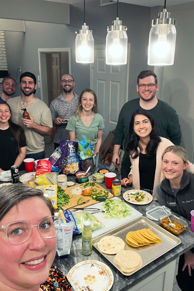Male and female fellows and faculty around a kitchen island filled with food