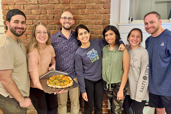 Three male and four female residents posing outside with one holding a pizza