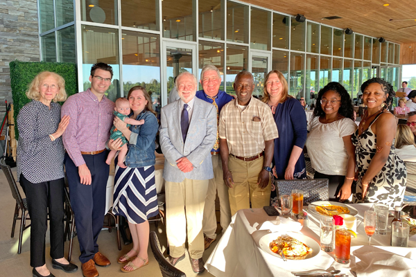 Group photo of fellow, family, and faculty at graduation in an outdoor setting