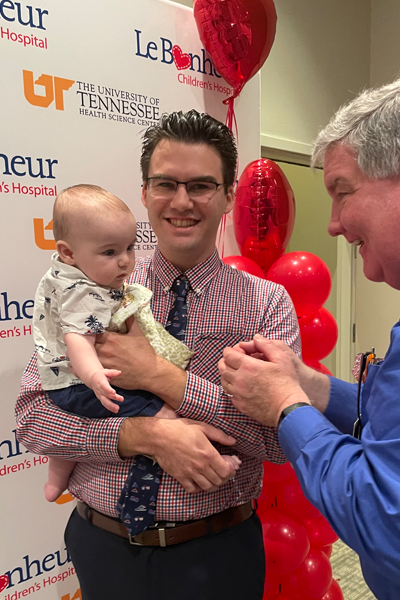 Graduate holding his child with a faculty member to the side