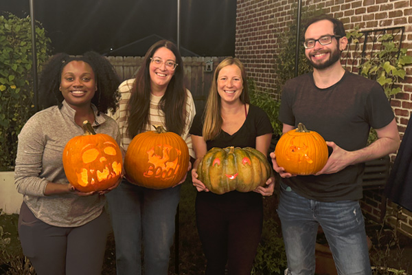 Four fellows standing outdoors at night holding carved pumpkins