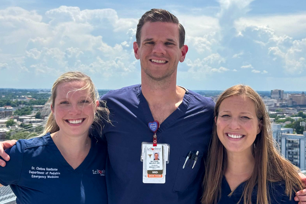 Three fellows in scrubs posing together outdoors with a city skyline in the background