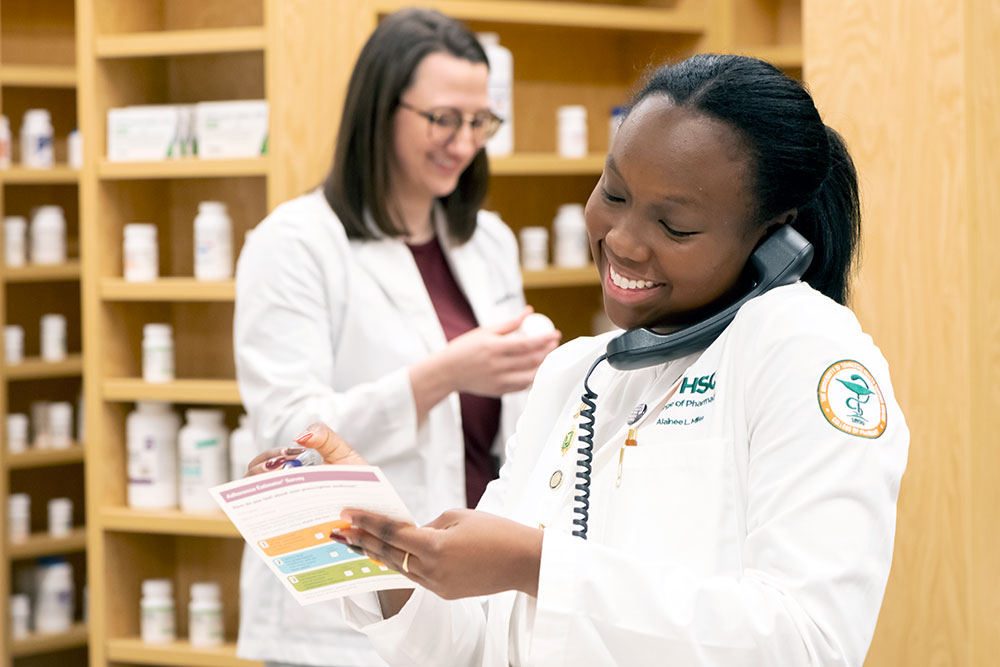 Pharmacy student answers phone in pharmacy setting.