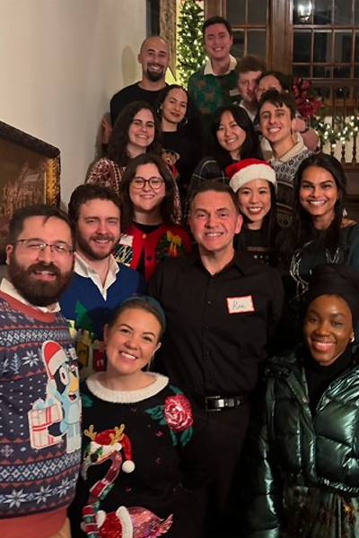 Residents and program director pose together at a holiday celebration, wearing festive sweaters and seasonal attire.