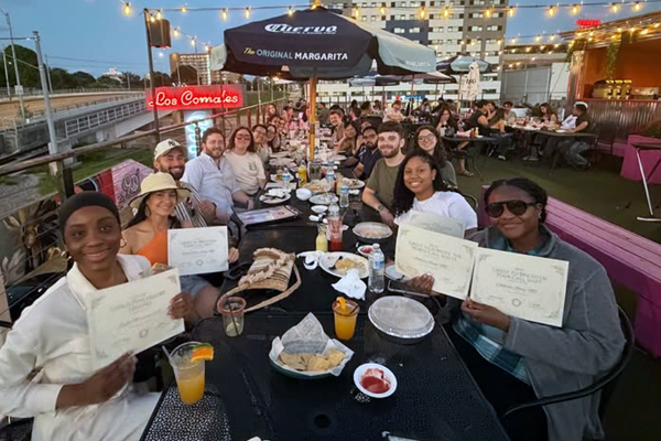 Residents seated together at long outdoor restaurant tables on a rooftop patio at dusk