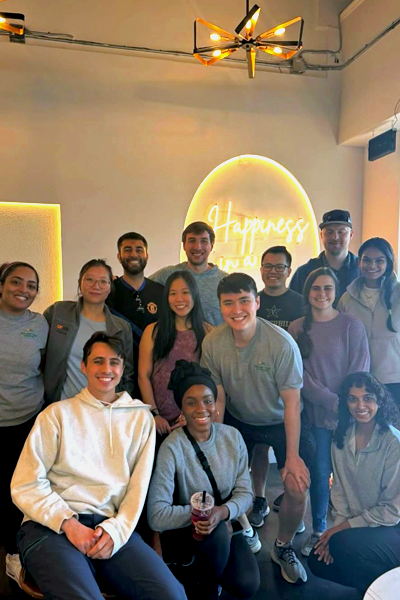 Group of residents pose for a photo inside a café beneath a glowing wall sign and modern lighting fixtures