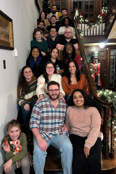 Residents gather on a decorated staircase inside a historic home adorned with holiday lights and garland